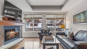 A cozy living room with a fireplace, leather sofas, and large windows offering a view of a building with a sloped roof.