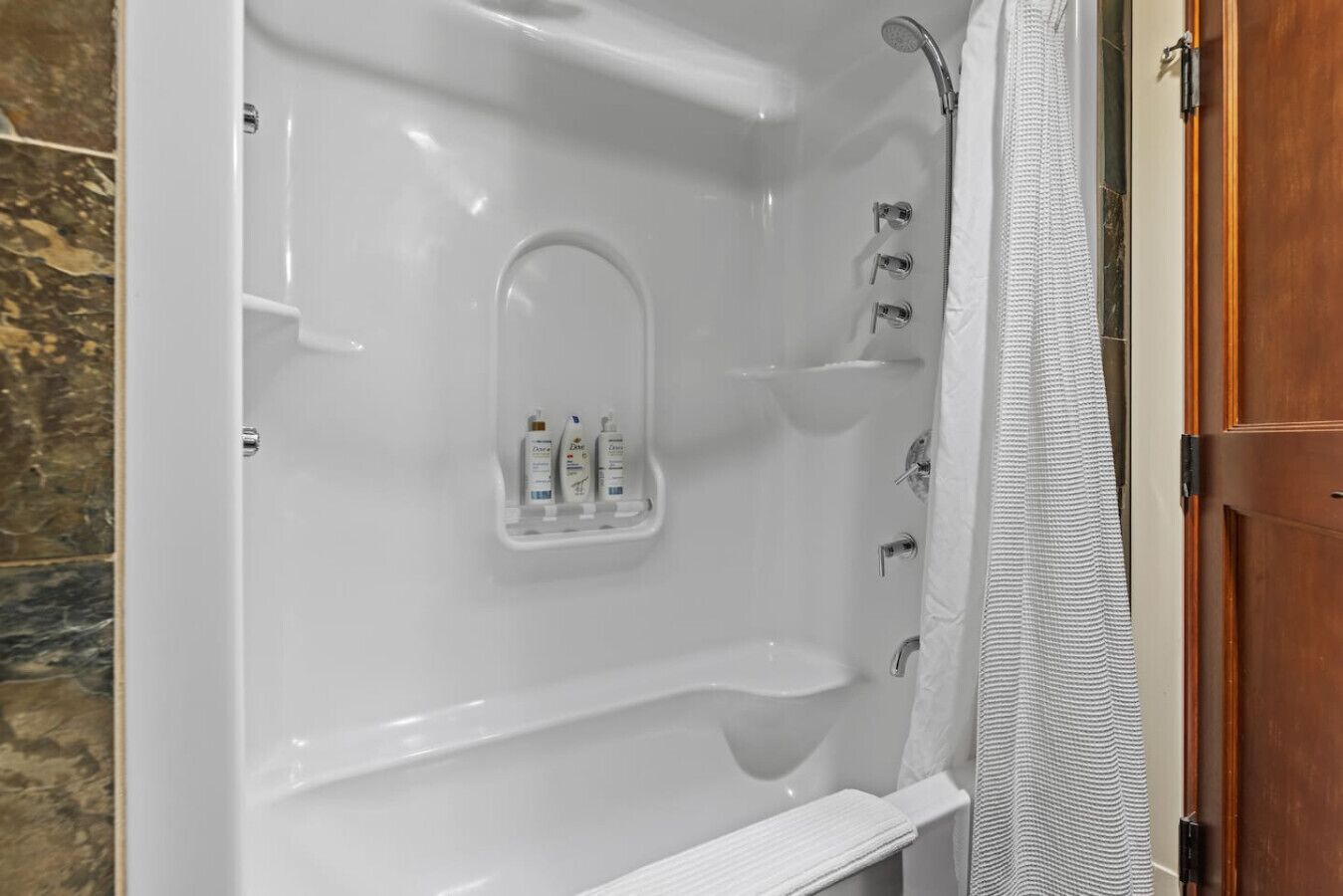Ein modernes Badezimmer mit Badewanne, Dusche und einer integrierten Ablage für Pflegeprodukte.