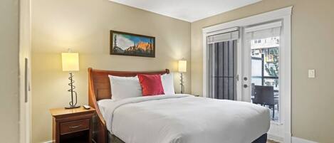A bedroom with a bed, two bedside lamps, a nightstand, a door to a balcony, and a painting on the wall.