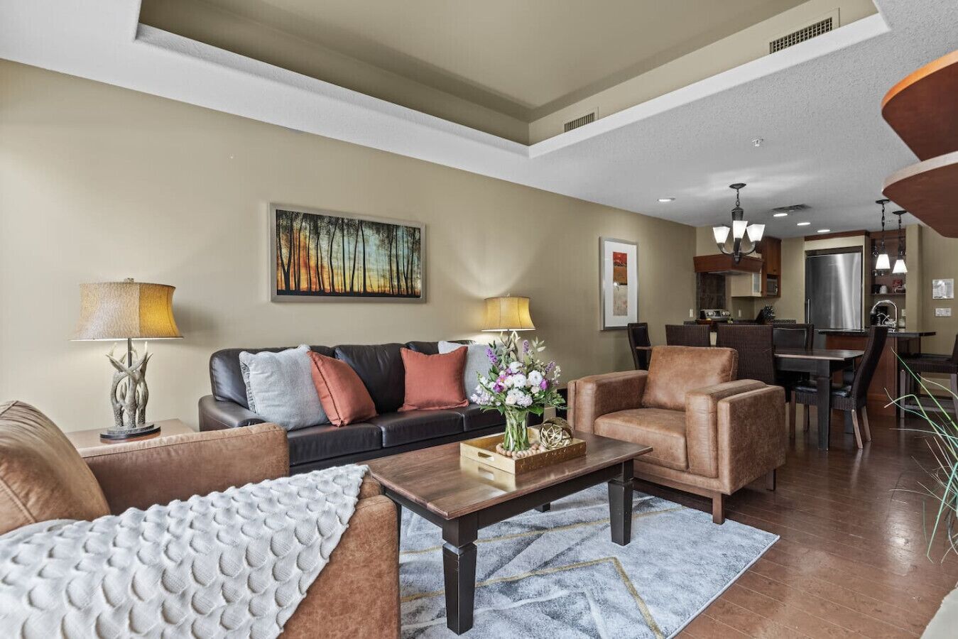A modern living room with a sofa, armchairs, a coffee table, and a dining area in the background.