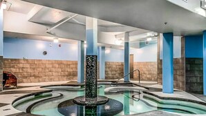 Una piscina interior con una fuente central, rodeada de paredes azules y beige, y sostenida por columnas.