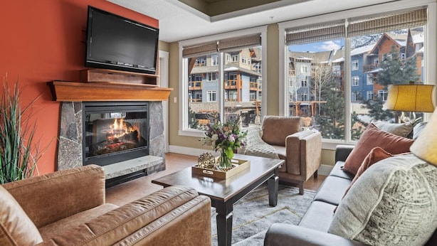 Un salón con chimenea, televisor de pantalla plana y un ventanal con vistas a una zona residencial.
