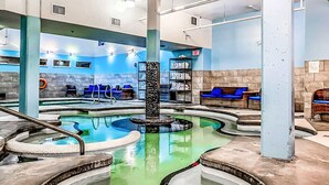 A pool area with multiple hot tubs, lounge chairs, and a central column.