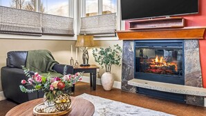 A living room with a fireplace, a sofa, a coffee table with flowers, and a TV mounted on the wall.