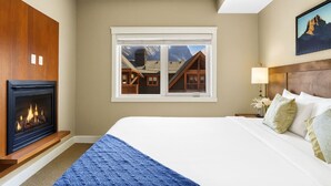 Un dormitorio con chimenea, una cama grande, un ventanal con vistas a la montaña y un cabecero de madera.
