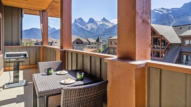 Un balcón con mobiliario de mimbre, una parrilla y vistas a montañas nevadas.