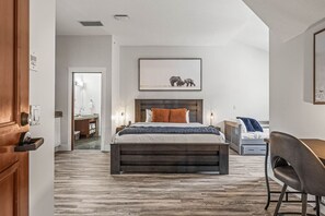 A bedroom with a wooden bed, a desk, and a chair. There is a bathroom visible in the background. - Mountain View Penthouse with Pool & Hot Tub (Canmore)