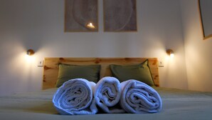 Ein ordentlich bezogenes Bett mit aufgerollten Handtüchern und zwei grünen Kissen.