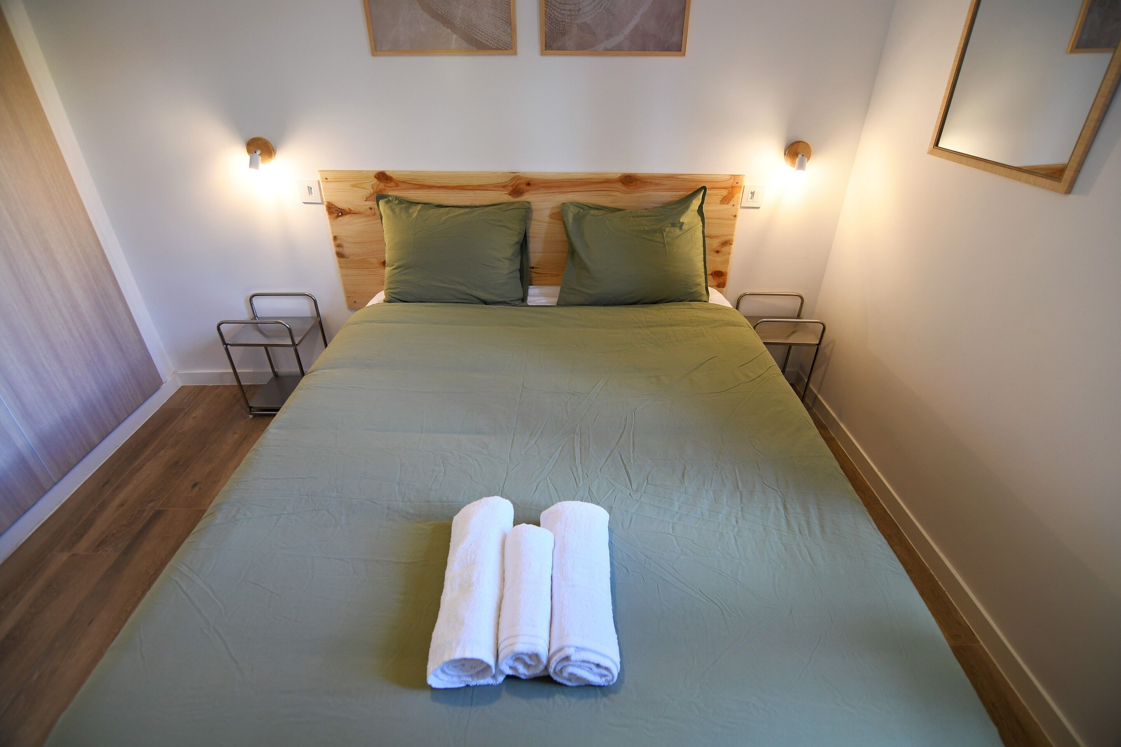 Una cama bien hecha con una colcha verde y dos almohadas, dos mesitas de noche con lámparas y un cabecero de madera.