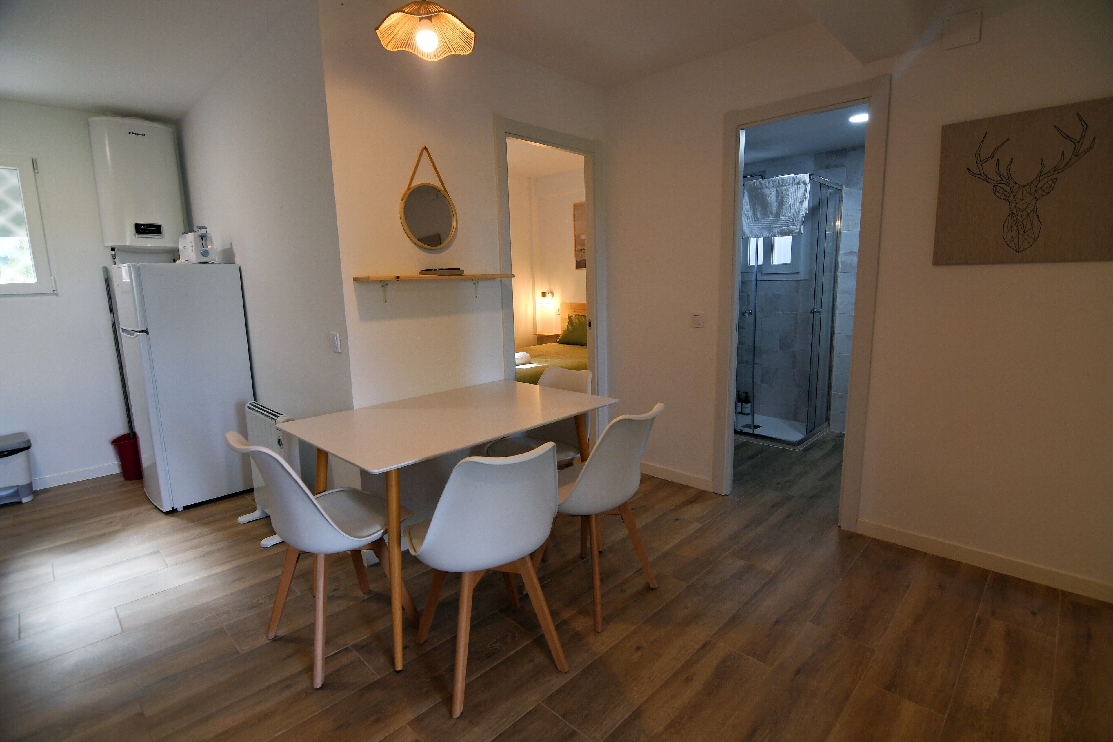 Eine moderne Küche mit einem weißen Kühlschrank, einem Esstisch mit vier Stühlen und einer hängenden Leuchte.