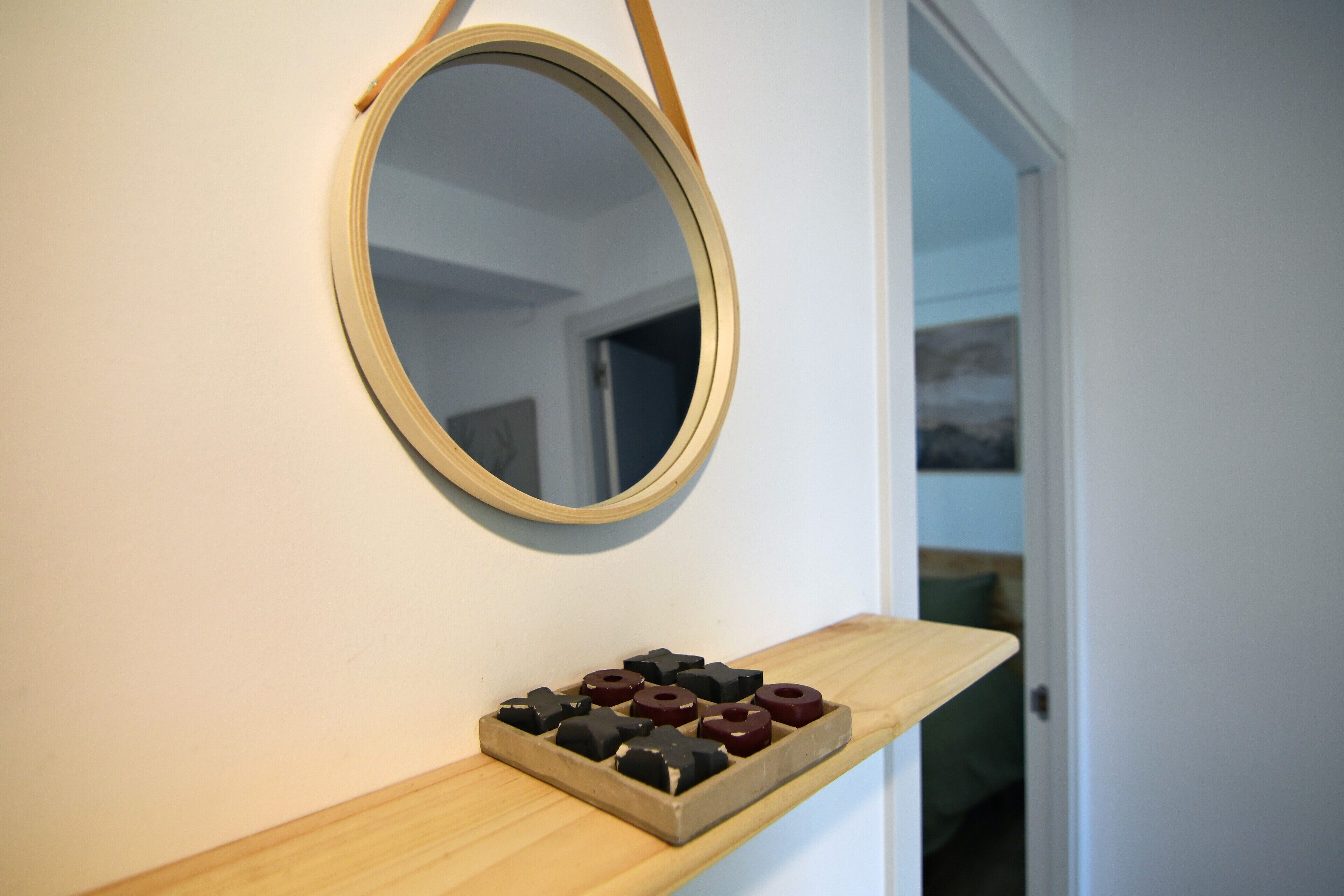 A mirror on a wall with a shelf below it holding several black and red objects.