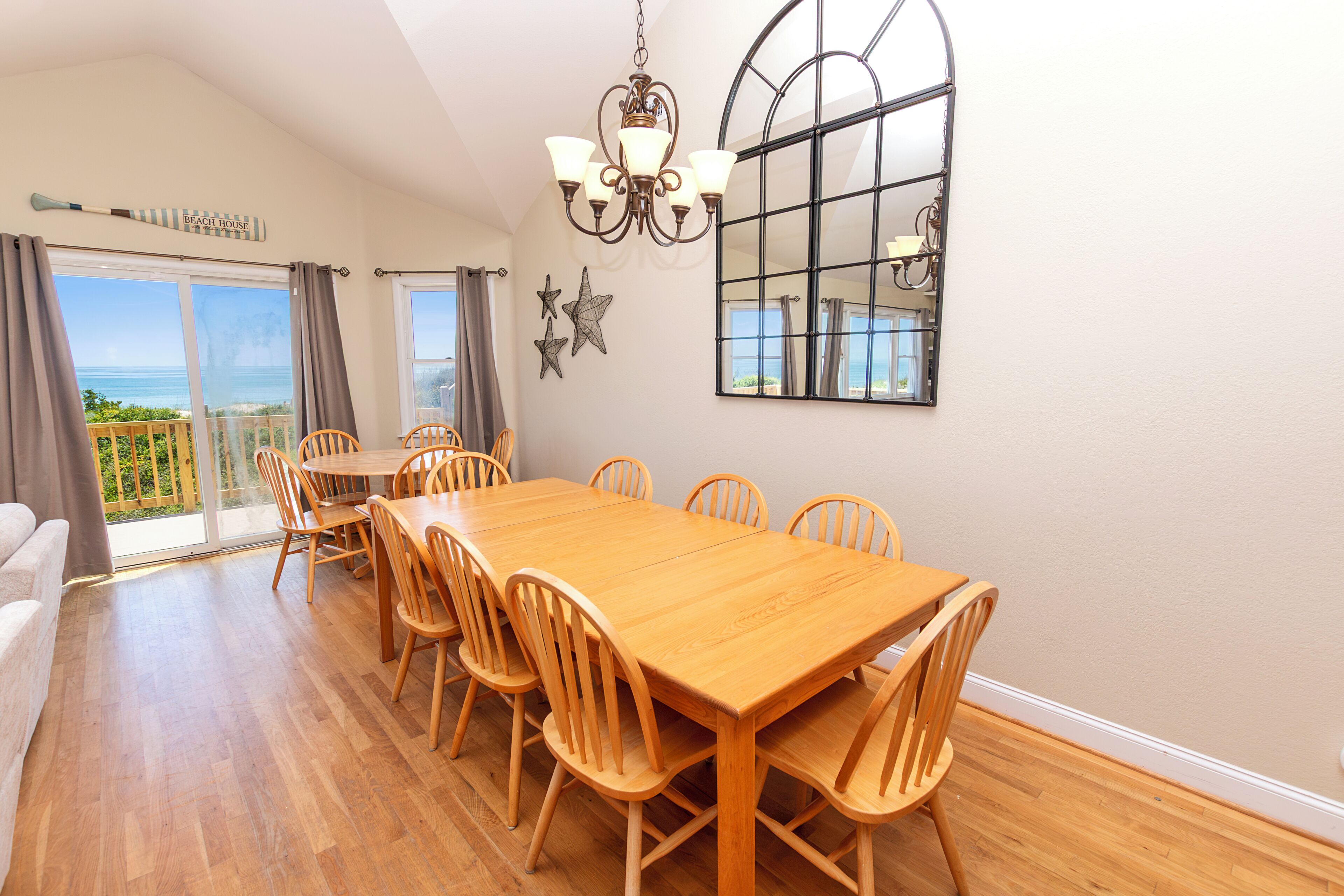 A dining area with a wooden table and chairs, a chandelier, and a large window with a view.
