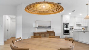 Een moderne keuken met witte kasten, een ronde houten tafel en een geweven hanglamp.