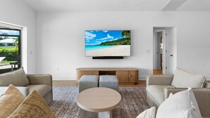 Een moderne woonkamer met een grote flatscreen televisie aan de wand, een houten tv-meubel, twee banken, een ronde salontafel en een kamerkleed met een patroon.