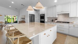 Een moderne keuken met witte kasten, een groot eiland, roestvrijstalen apparatuur en hanglampen.