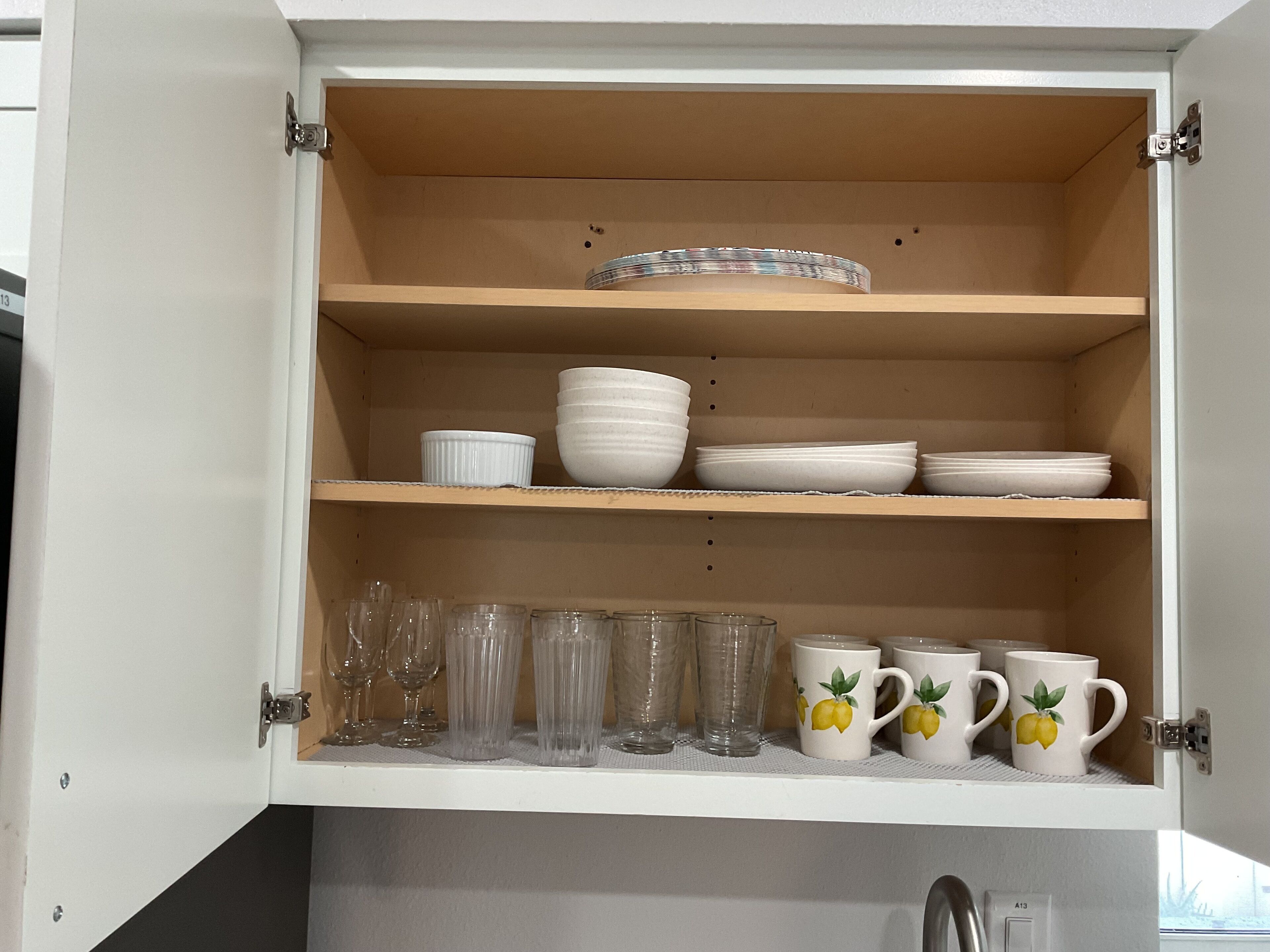 Un meuble de cuisine avec des étagères contenant des bols blancs, des assiettes et des verres transparents.