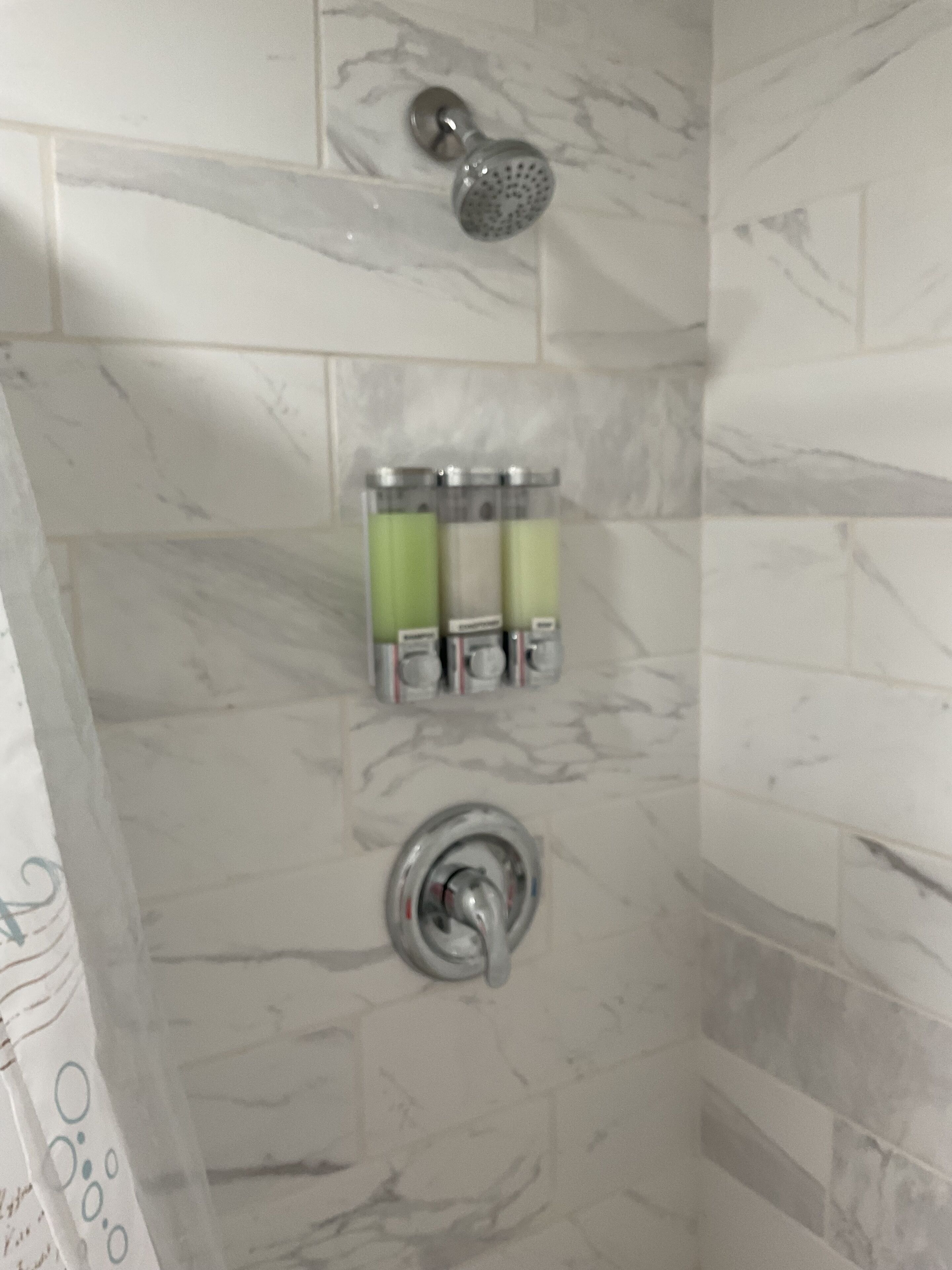 Une salle de bain avec une douche, des carreaux de marbre et un distributeur de savon.