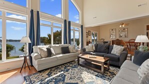 A spacious living room with large windows, a blue patterned rug, and two sofas.