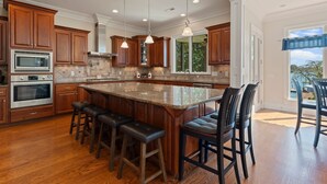 A spacious kitchen with wooden cabinets, a large island with bar stools, stainless steel appliances, and pendant lighting.