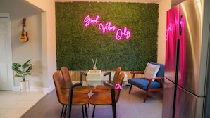 A modern living room with a green wall, a neon sign, a guitar, a plant, and a dining area. - Chic-Miami GoodVibesOnly – Mins to Brickell & Beaches (Miami)