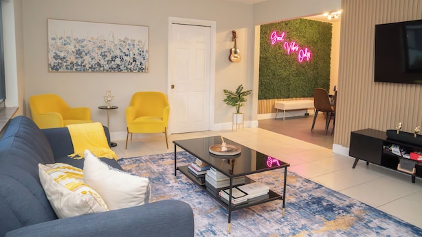 A modern living room with a sofa, coffee table, and chairs. There is a television, a guitar, and a neon sign. - Chic-Miami GoodVibesOnly – Mins to Brickell & Beaches (Miami)