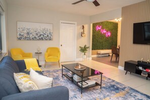 A modern living room with a sofa, coffee table, and chairs. There is a television, a guitar, and a neon sign. - Chic-Miami GoodVibesOnly – Mins to Brickell & Beaches (Miami)