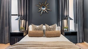 Una camera da letto con un letto grande, due comodini, uno specchio a forma di stella fissato alla parete e tende grigie.