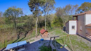 Un cortile recintato con altalena, un piccolo capanno di legno e una panchina.