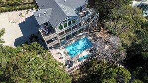 A multi-story house with a large swimming pool, surrounded by trees and a deck. - Once Upon a Tide: Stunning Soundfront, Private Pool, Hot Tub, Private Dock (Corolla)