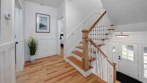 A staircase with wooden steps and white railings, leading to a landing with a door and a window. - Once Upon a Tide: Stunning Soundfront, Private Pool, Hot Tub, Private Dock (Corolla)