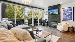 A modern living room with a fireplace, a large window, and a view of the outdoors. - 2BR Walk to Ski - Spa-like Bath (Park City)