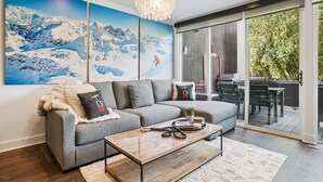 A modern living room with a grey sofa, a wooden coffee table, and a large painting of a snowy mountain landscape. - 2BR Walk to Ski - Spa-like Bath (Park City)