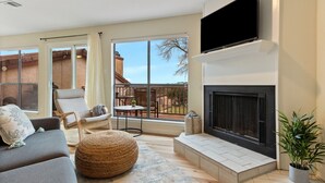 A modern living room with a fireplace, comfortable seating, and a large window offering a view of the outdoors. - Lake & Hill Country Views, 2 Master Suites, Pet Friendly, Deck w/ Grill (Canyon Lake)