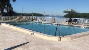 A swimming pool with a tiled deck, a metal railing, and a view of the sea. - Charming 2-bedroom condo overlooking Sarasota Bay on Longboat Key (Longboat Key)
