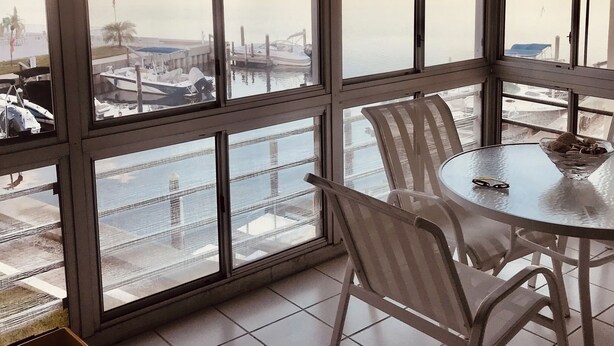 A room with large windows overlooking a body of water, a dining table with chairs, and a ceiling fan. - Charming 2-bedroom condo overlooking Sarasota Bay on Longboat Key (Longboat Key)
