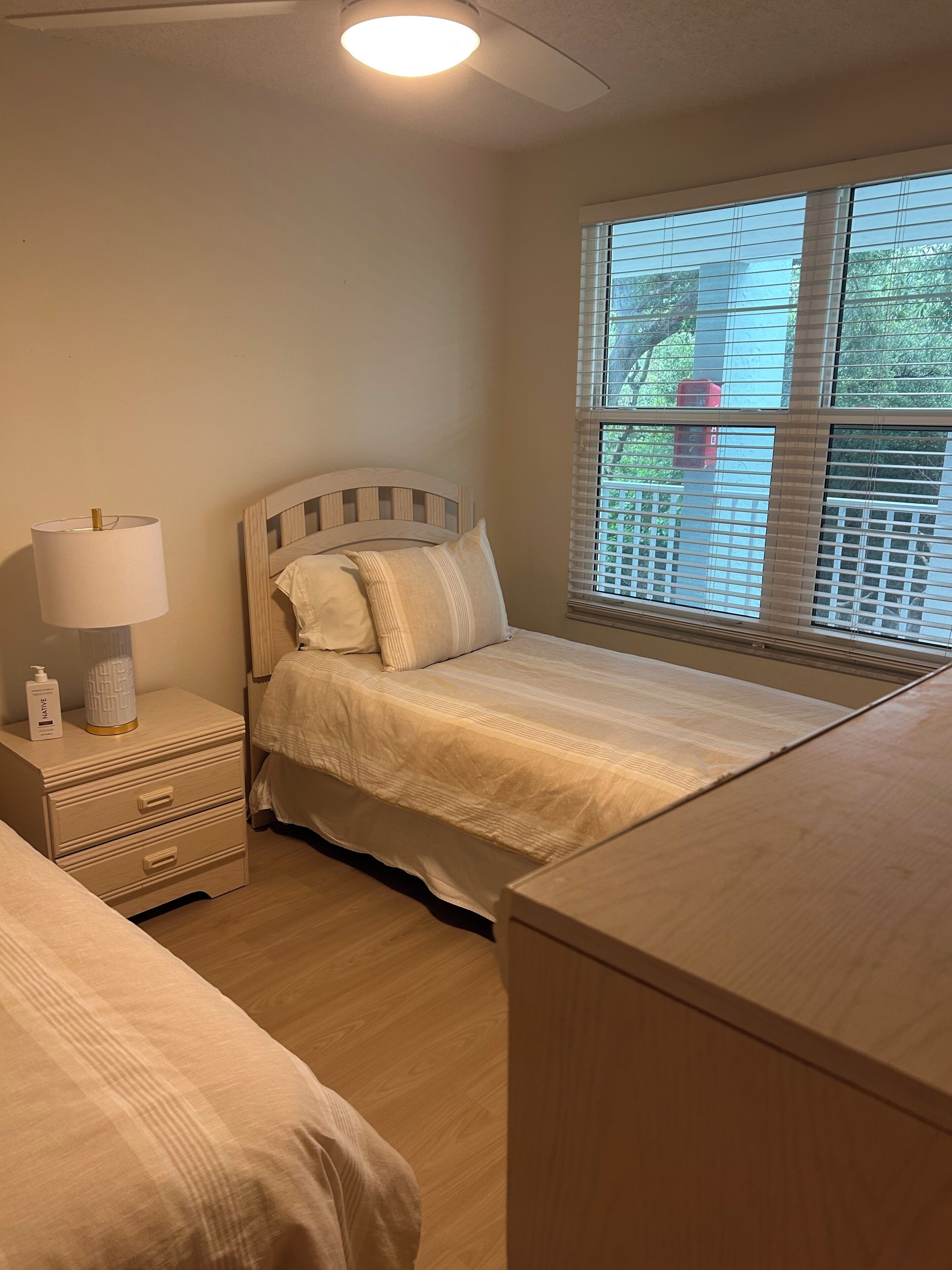 A bedroom with a bed, bedside table, lamp, and a window with blinds.