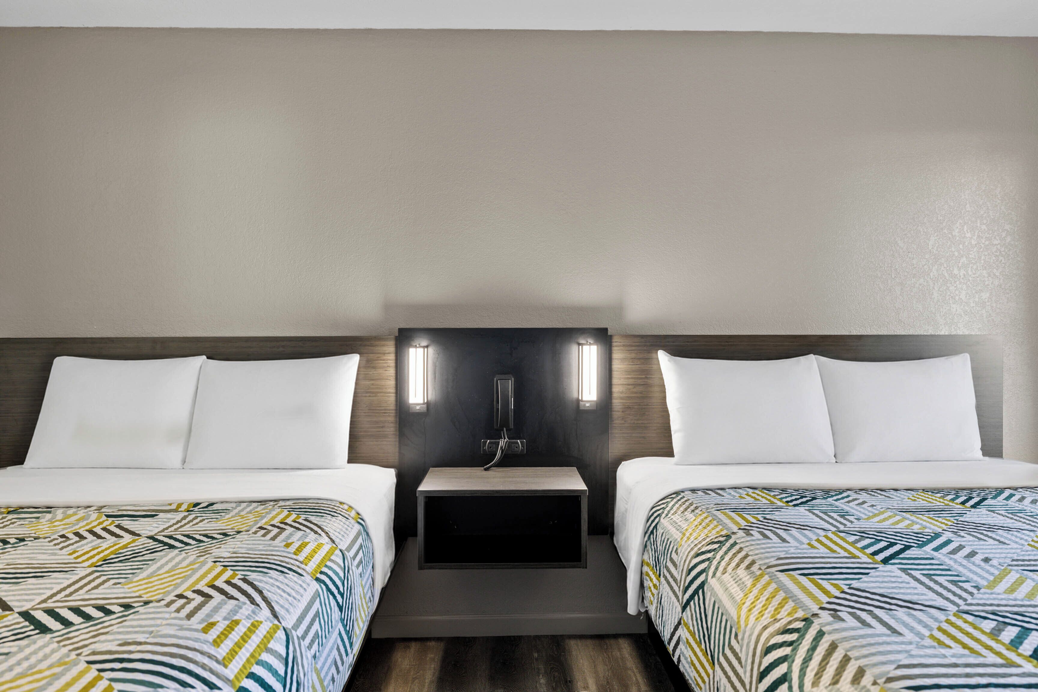Habitación de hotel con dos camas, una mesita de noche y un teléfono en la pared.