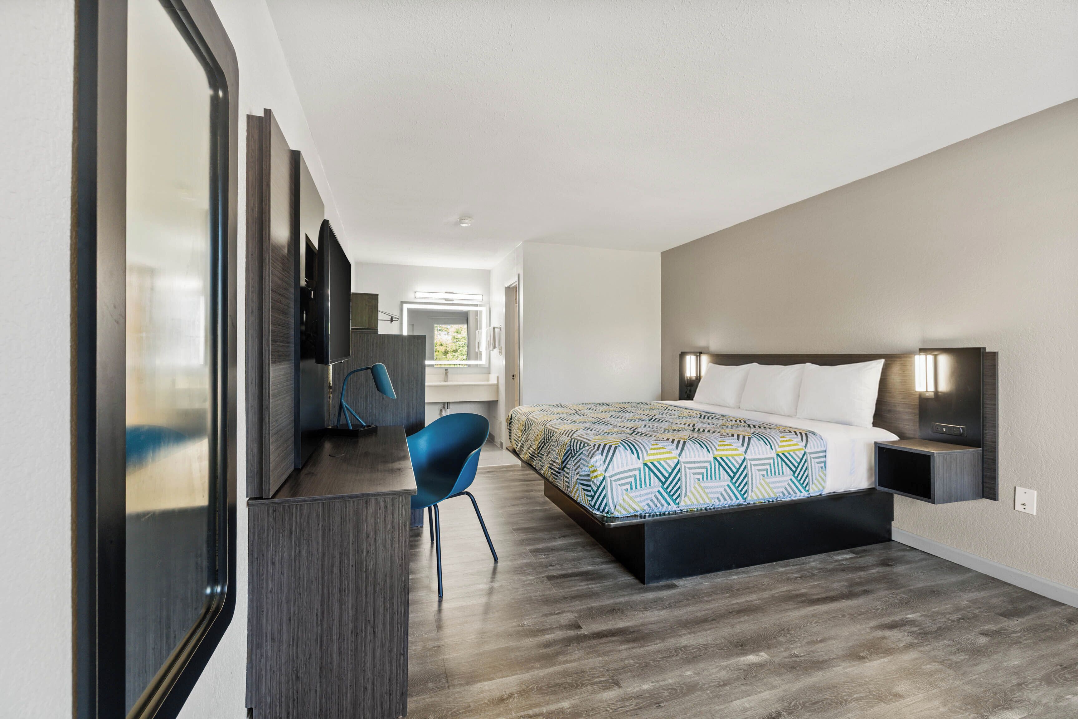A modern hotel room with a large bed, a desk, and a chair.