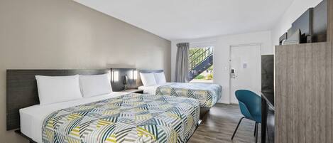 Habitación de hotel con dos camas, un escritorio y una silla. Se ve una ventana con vista a una escalera y follaje exterior.