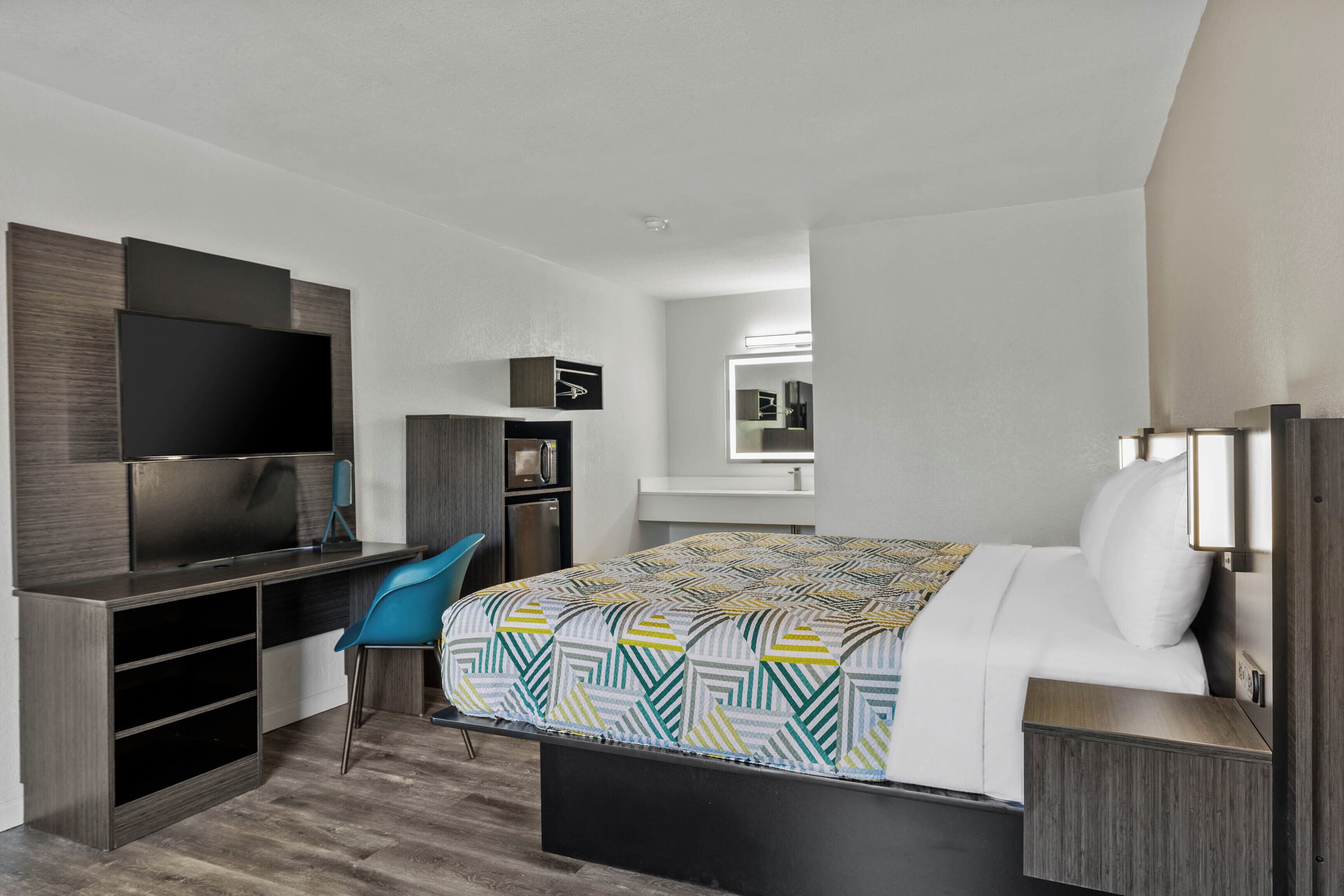 Une chambre d’hôtel équipée d’un lit, d’un bureau, d’une chaise, d’une télévision et d’un miroir.