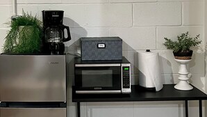 A kitchenette with a stainless steel refrigerator, a microwave, and a coffee maker on a black countertop. There is a basket under the microwave and a potted plant on the countertop. - Hotel-Style Retreat on private property - Sleeps 4 (Three Rivers)