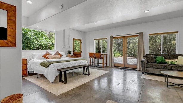 A spacious bedroom with a large bed, a bench, a sofa, and a dining area. - Hotel-Style Retreat on private property - Sleeps 4 (Three Rivers)