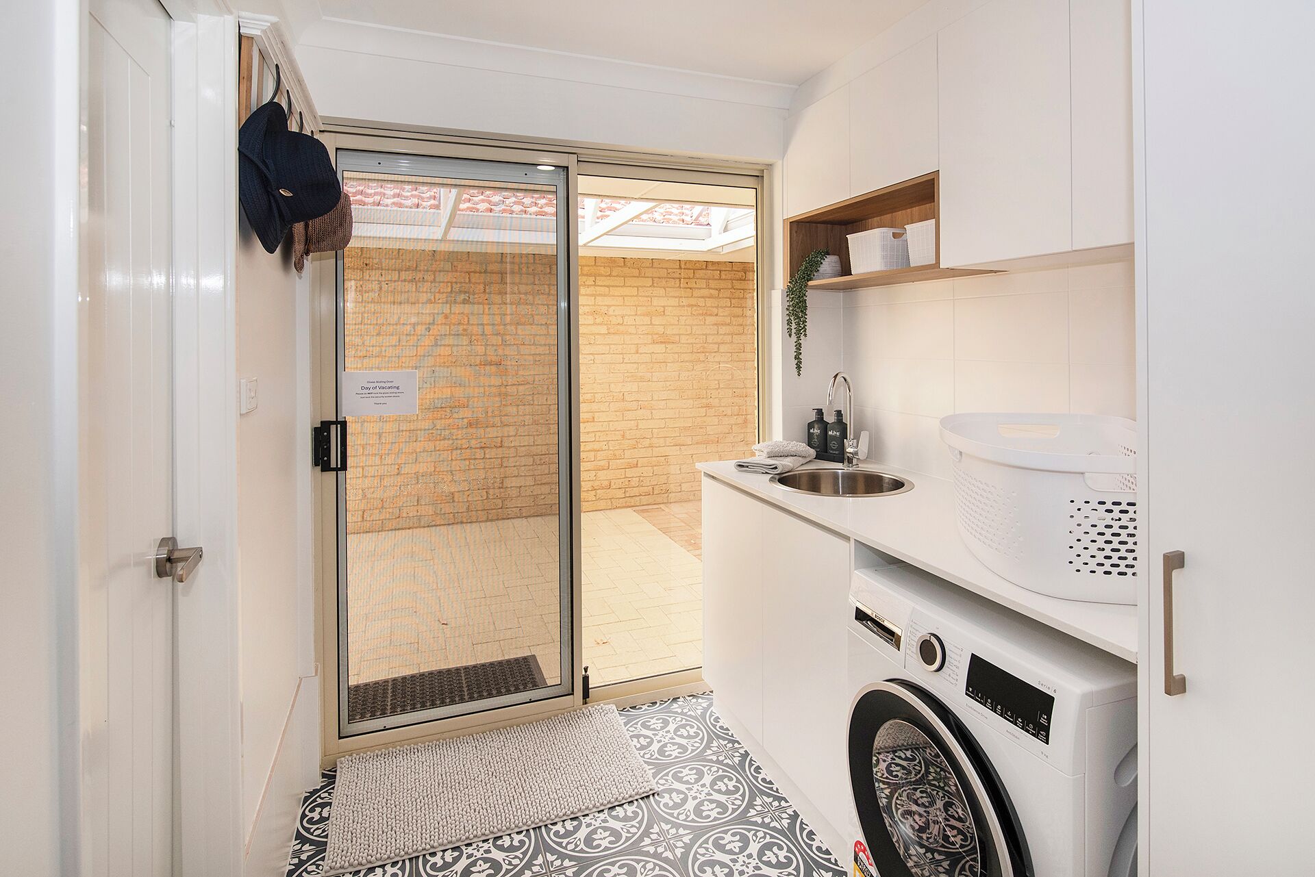 A compact laundry room with a washing machine, a sink, and a drying rack.
