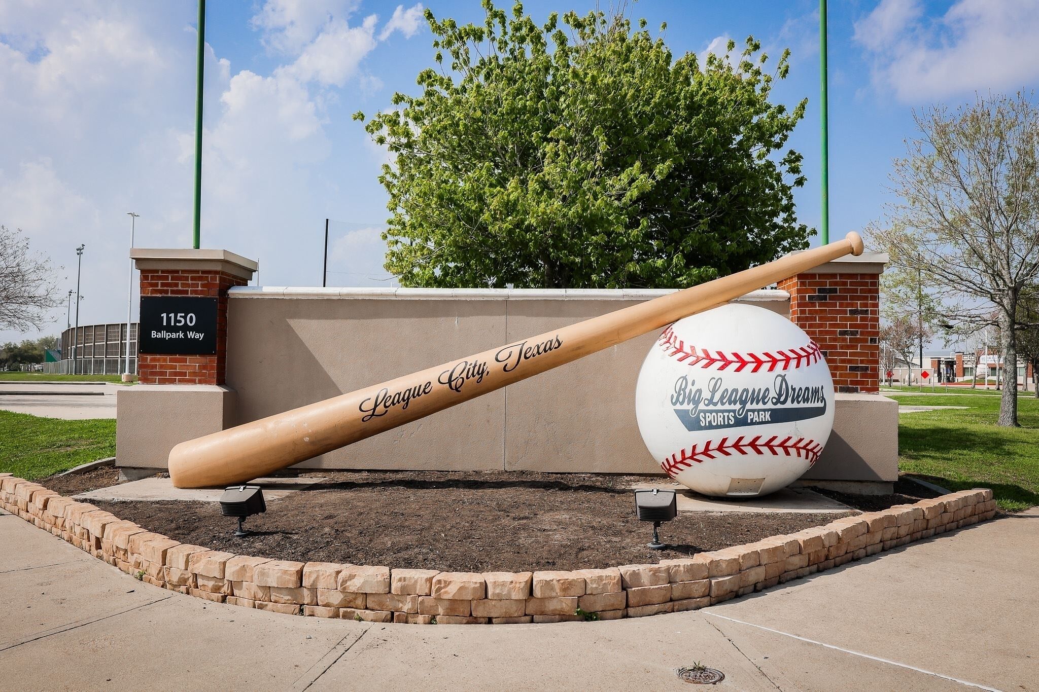A baseball bat and ball sculpture at a sports park entrance.