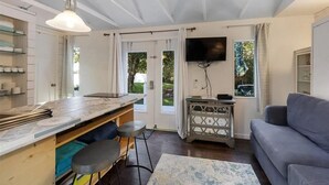 A modern kitchen with a bar area, a grey sofa, and a flat-screen TV mounted on the wall. - Tiny house 5 minutes near Kemah boardwalk! (Bacliff)