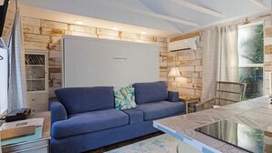 A modern living room with a sofa, a glass coffee table, and a bookshelf. - Tiny house 5 minutes near Kemah boardwalk! (Bacliff)