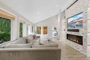 A modern living room with a sectional sofa, a fireplace, and a large TV mounted on a brick wall. - Warm Springs Getaway | Hot Tub | Near Lift & Downtown (Ketchum)