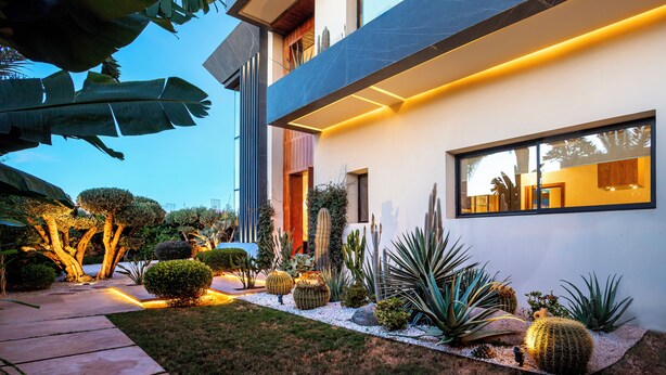 Ein modernes Haus mit einem gepflegten Garten, einschließlich Kakteen und anderer Pflanzen, und einem wolkenlosen Himmel.