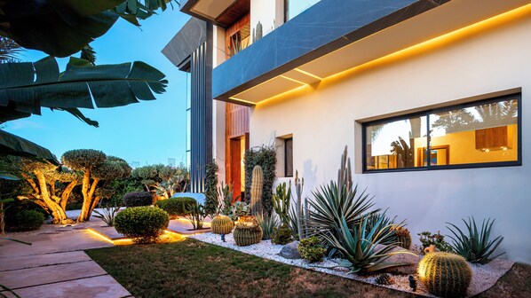 Una casa moderna con un jardín bien cuidado, que incluye cactus y otras plantas, bajo un cielo despejado.