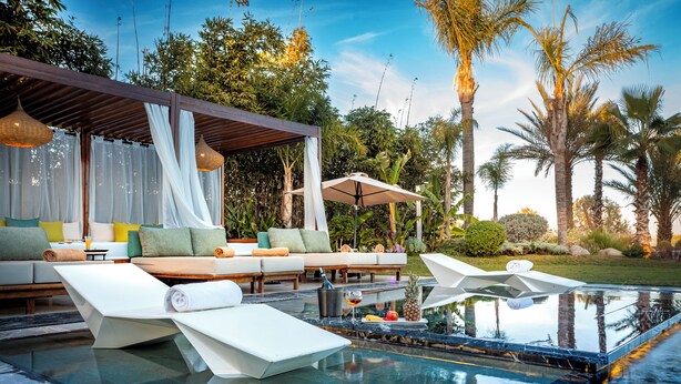 An infinity pool with lounge chairs, a covered seating area, and tropical vegetation. - Villa Harmonie Luxe & Bien-être in the golf residence with spa (Marrakech)